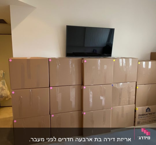 קופסאות קרטון מסודרות בערימה ליד טלוויזיה על קיר